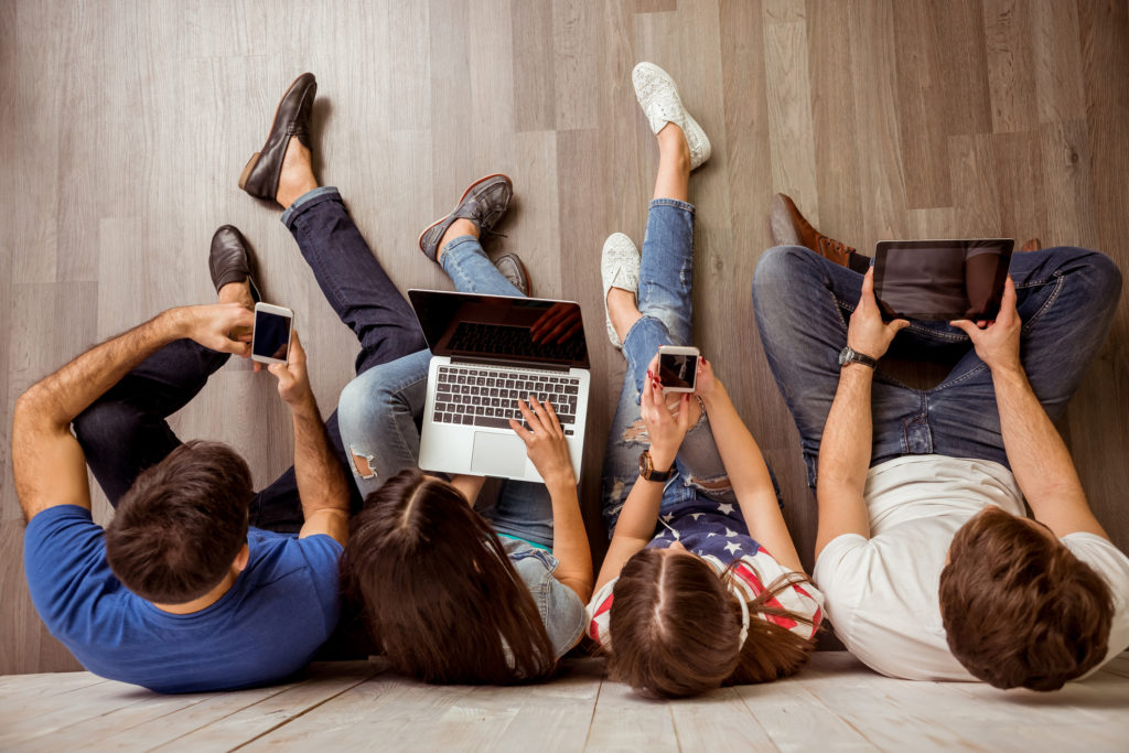 Group of attractive young people sitting on the floor using a laptop, Tablet PC, smart phones, headphones listening to music