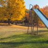 A colorful playground in the fall with a metal slide in the foreground.