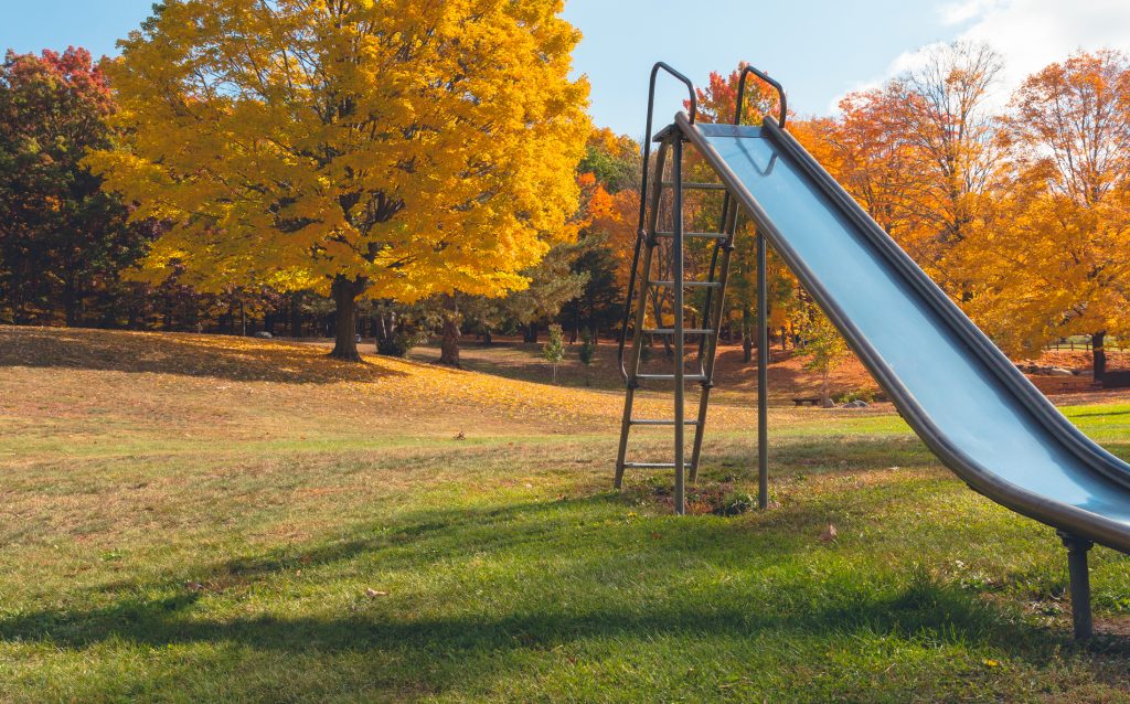 A colorful playground in the fall with a metal slide in the foreground.