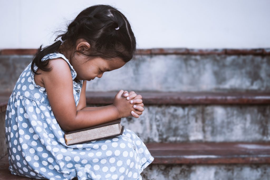Cute little girl closed her eyes and folded her hand in prayer on a Holy Bible