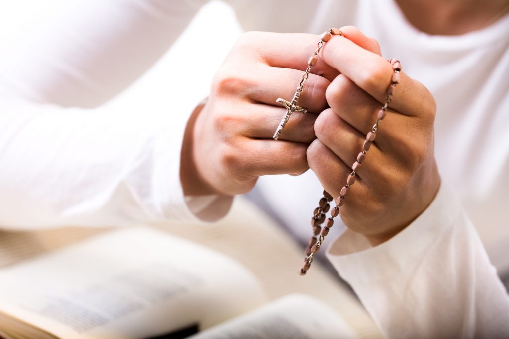 Woman praying, holding rosary beads over bible