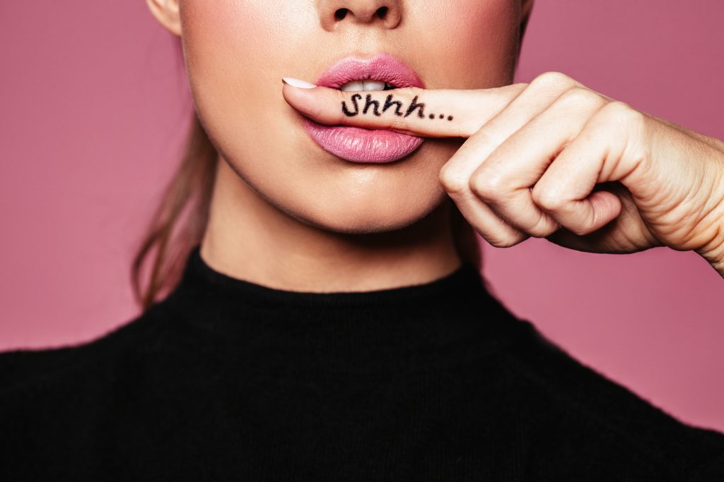 female with finger in mouth showing a sign of silence with shhh written on the finger.