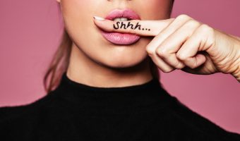 female with finger in mouth showing a sign of silence with shhh written on the finger.