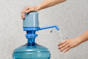 closeup of hands pumping water into glass from bottle