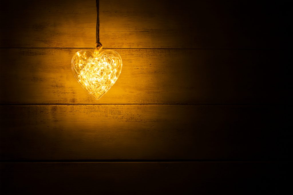 Hanging warm glowing orange heart on a wooden background