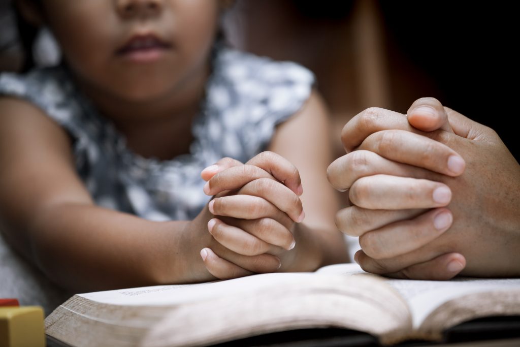 Mother and little girl hands folded in prayer on a Holy Bible together