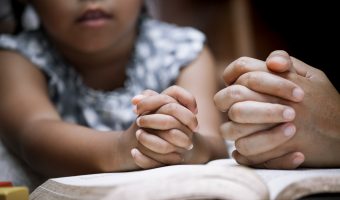 Mother and little girl hands folded in prayer on a Holy Bible together