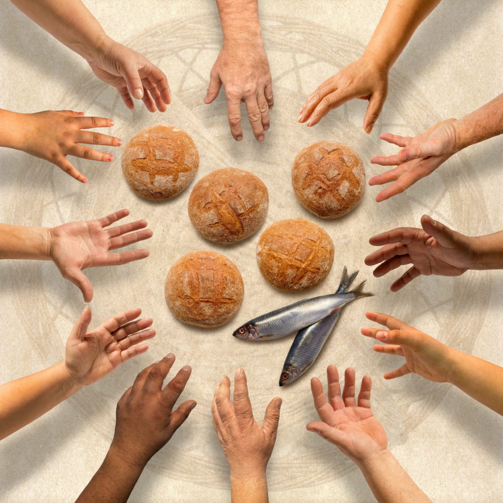 Hands stretching around five small barley loaves and two small fish