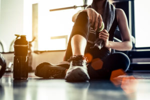 Sport woman sitting and resting after workout or exercise in fitness gym with protein shake or drinking water on floor. Strength training 