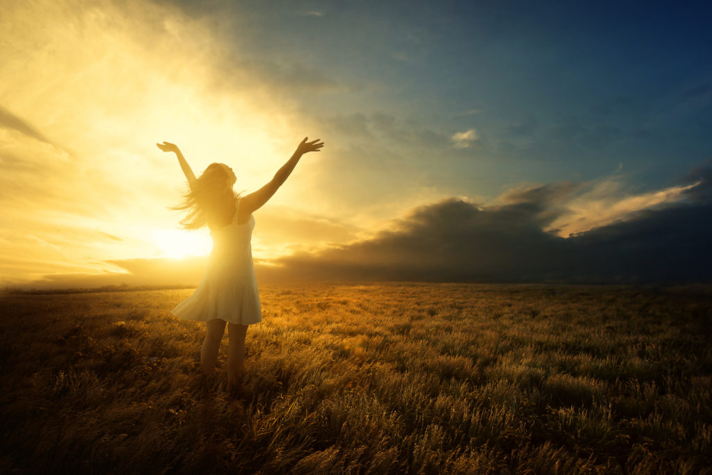 A woman lifts her arms in praise at sunset